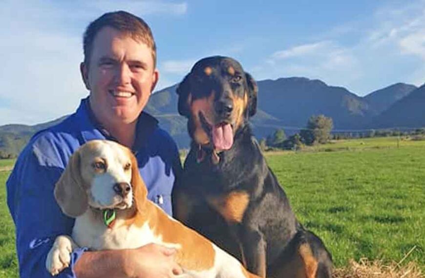 Farmer Wayne Langford sits with two working dogs in a field