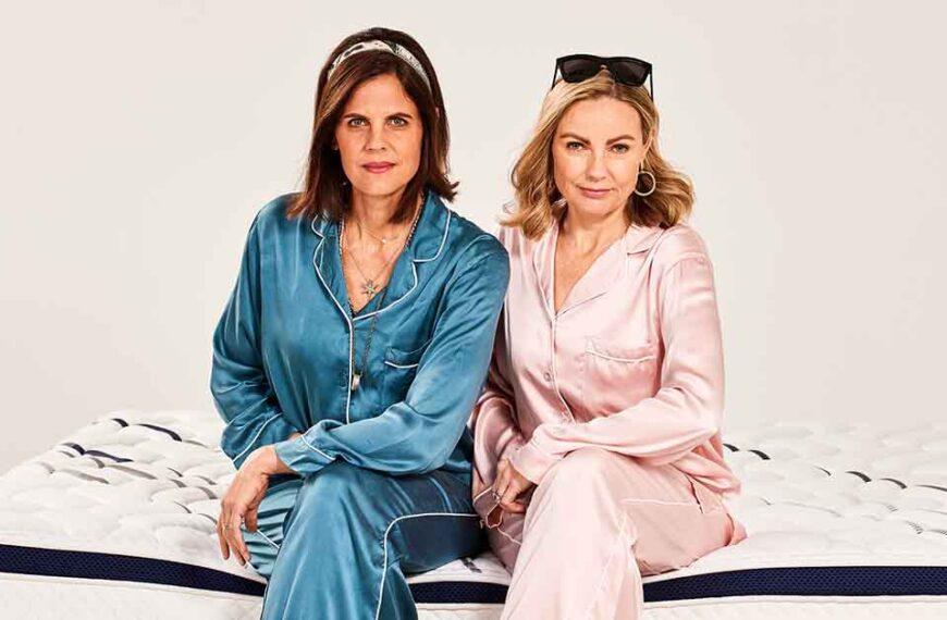 Vicki Eriksen (left) and Susie Harris sit on a bed wearing pyjamas.