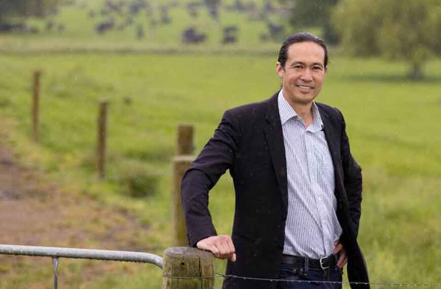 LIC chief executive David Chin leans on a farm gate with paddocks and a raceway behind him.