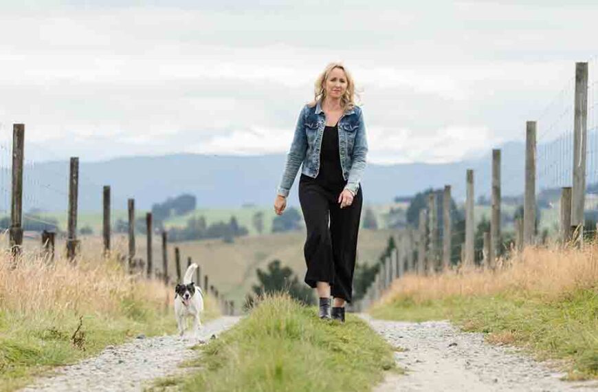 Kathryn Wright walks towards the camera down a farm track with a small dog by her side.