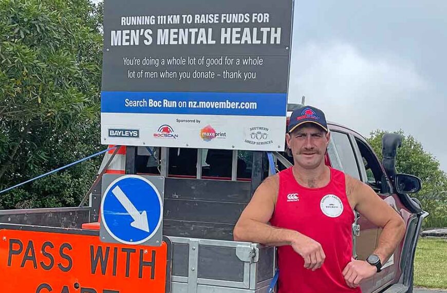 Ben O'Carroll stands leaning on a ute in his running gear. A sign says "raising funds for men's mental health" behind him.