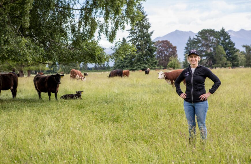 Woman standing in a paddock with cows in the background.